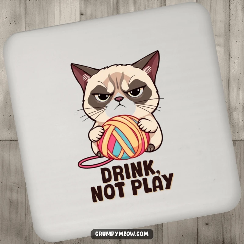 Funny grumpy cat with narrowed eyes, judging a brightly colored ball of yarn on a drink coaster, a stylish funny gift.