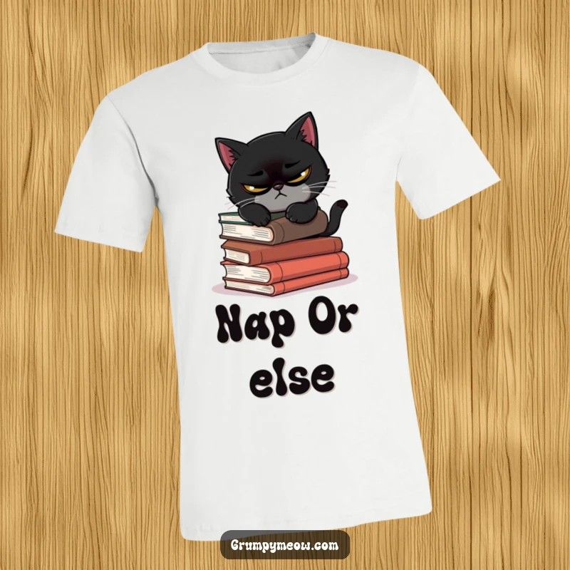 Funny t-shirt of a scowling black cat attempting to nap on a stack of precarious books, capturing its struggle.